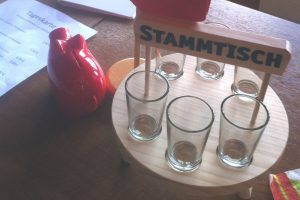 Stammtisch mit sechs kleinen Gläsern auf einem Holttablett neben einem roten Sparschwein