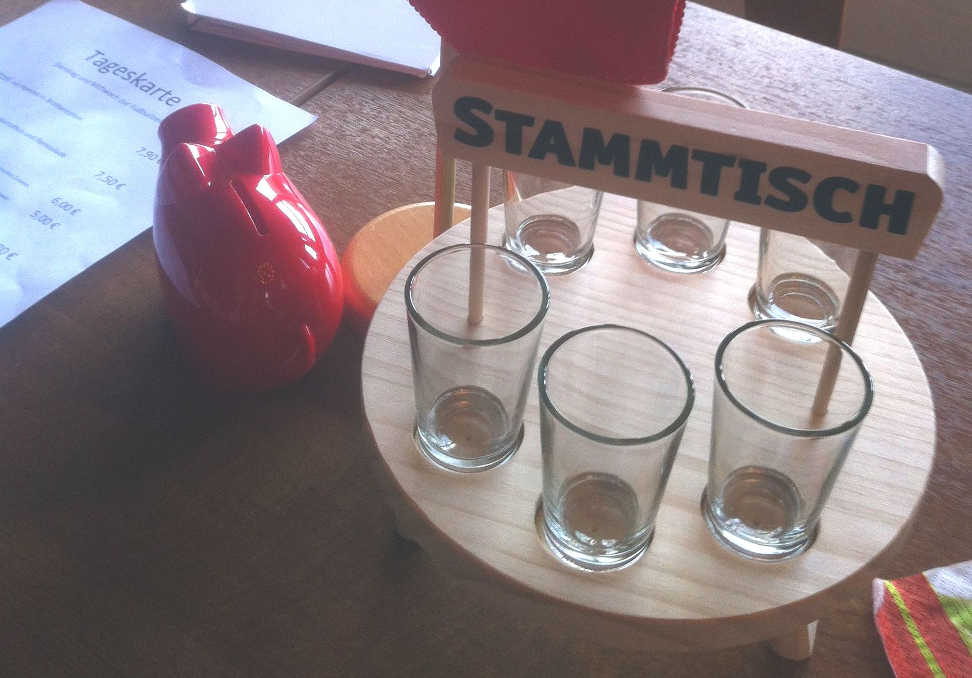 Stammtisch mit sechs kleinen Gläsern auf einem Holttablett neben einem roten Sparschwein