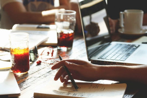Laptop, Notizblöcke, Getränke, Hände auf einem Tisch signalisieren gemeinsames Arbeiten