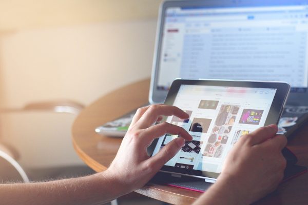 Hände tippen auf Tablet, Laptop im Hintergrund