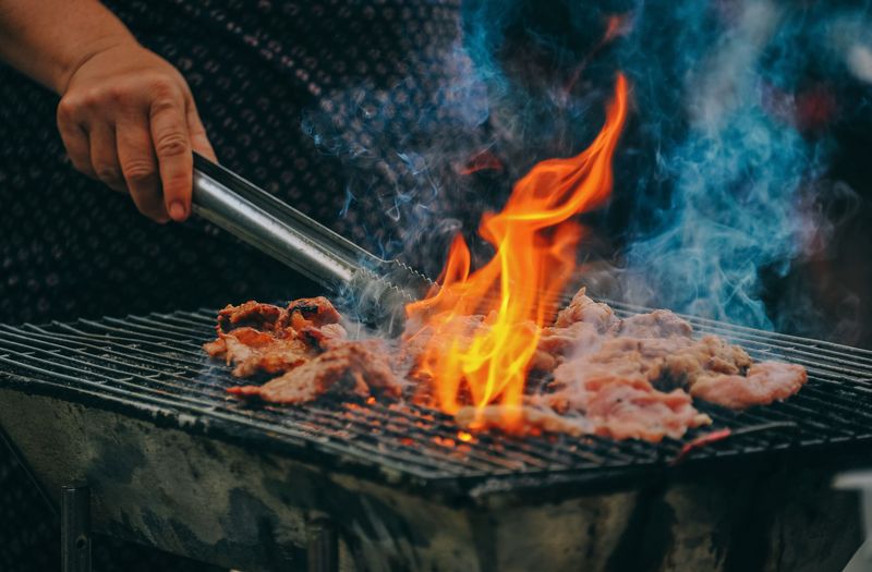 Mann wendet GFleisch auf Grill mit Zange um. Flamme lodert.