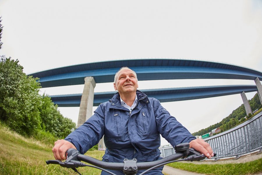 Mathias Stein auf dem Fahrrad, aufgenommen aus der Froschperspektive mit Brücke im Hintergrund.