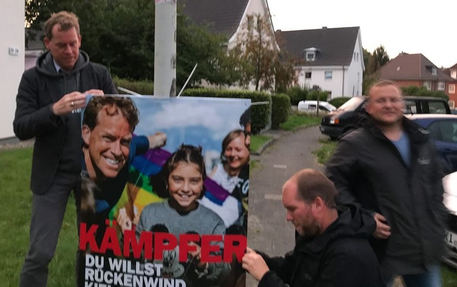 Drei Männer hängen ein Plakat auf