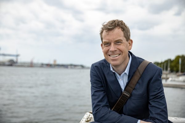 Ulf Kämpfer lächelt mit der Förde im Hintergrund