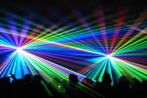 Eine Laser-Show/ein Lichterspiel bei Nacht, die sich eine unbestimmte Anzahl von Personen (nur als Silhouette sichtbar) ansehen