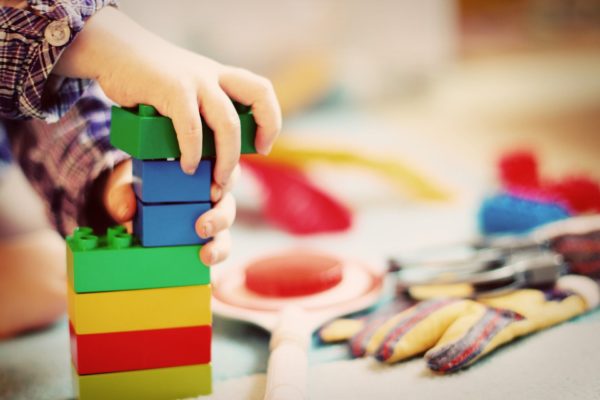 Kind baut mit Duplosteinen einen Turm. Spielzeug im Hintergrund.