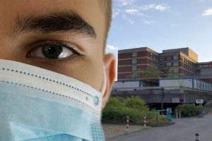Das Bild zeigt einen Mann mit Mundschutz im Vordergrund und im Hintergrund das Städtische Krankenhaus Kiel.