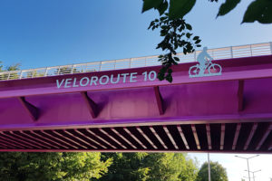 Lilafarbene Fahrrad-Brücke mit Buchstaben VELOROUTE 10 und ein Fahrradfahrer