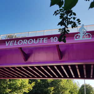 Lilafarbene Fahrrad-Brücke mit Buchstaben VELOROUTE 10 und ein Fahrradfahrer