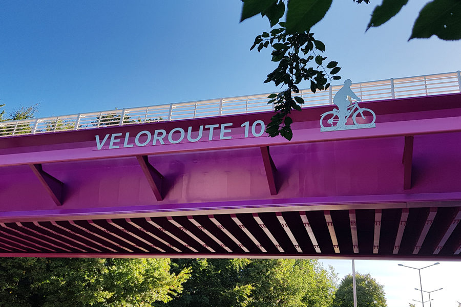 Lilafarbene Fahrrad-Brücke mit Buchstaben VELOROUTE 10 und ein Fahrradfahrer