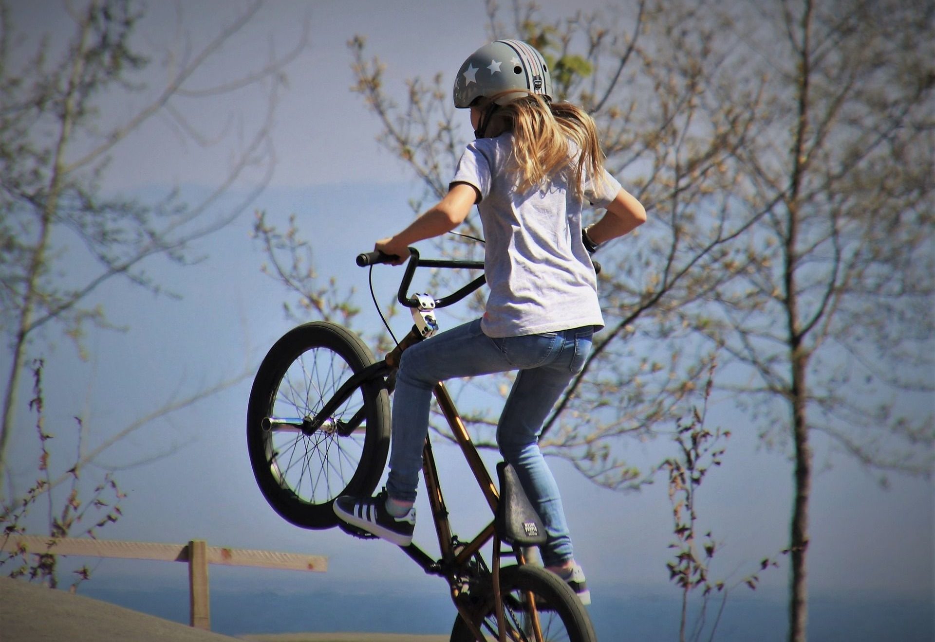 Mädchen mti Helm auf einem BMX-Rad in der Luft.