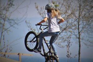 Mädchen mti Helm auf einem BMX-Rad in der Luft.
