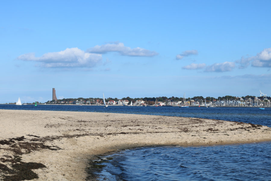 Das Foto zeigt den Falckensteiner Strand mit Blick auf die Kieler Förde. Im Hintergrund ist Laboe mit seinem Denkmal zu erkennen.