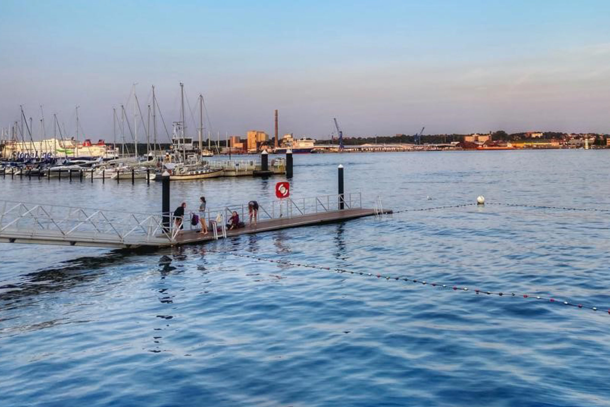 Das Foto zeigt einen Badesteg an der Kiellinie an den frühen sommerlichen Abendstunden. Im Hintergrund kann man die StenaLine und das Ostufer erkennen.