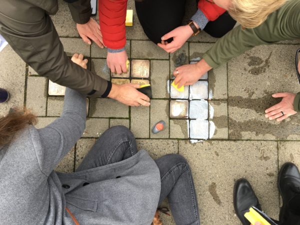 Mehrere Menschen putzen mit Schwämmen und Reinigungsmitteln in den Bürgersteig eingelassene Stolpersteine