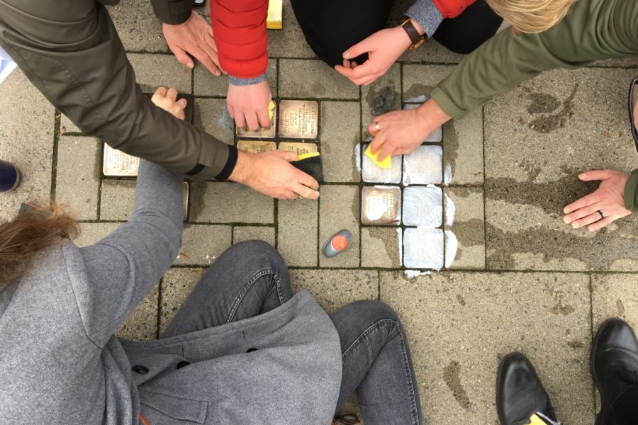 Mehrere Menschen putzen mit Schwämmen und Reinigungsmitteln in den Bürgersteig eingelassene Stolpersteine