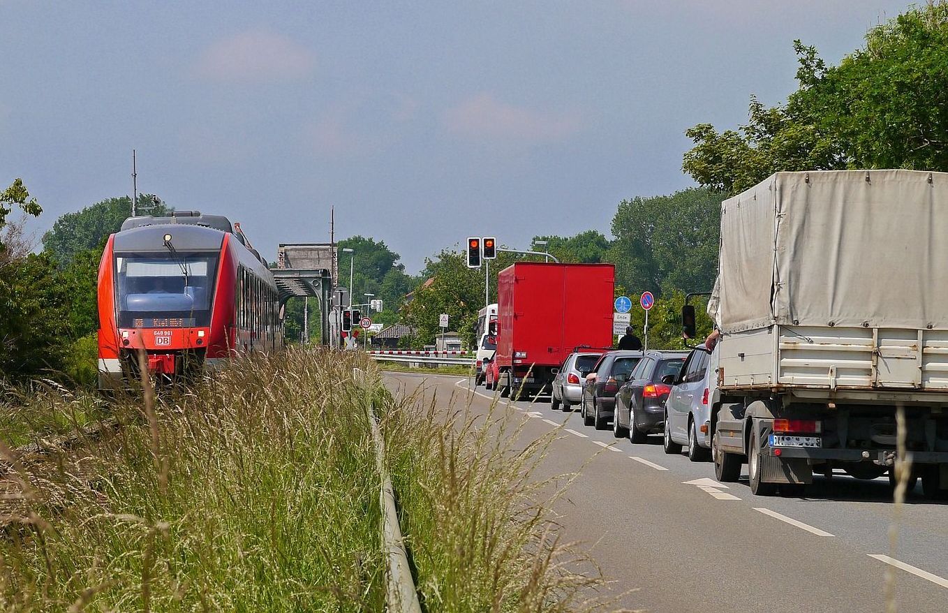 Zug auf einem Gleis neben einer Straße mit Autos im Stau