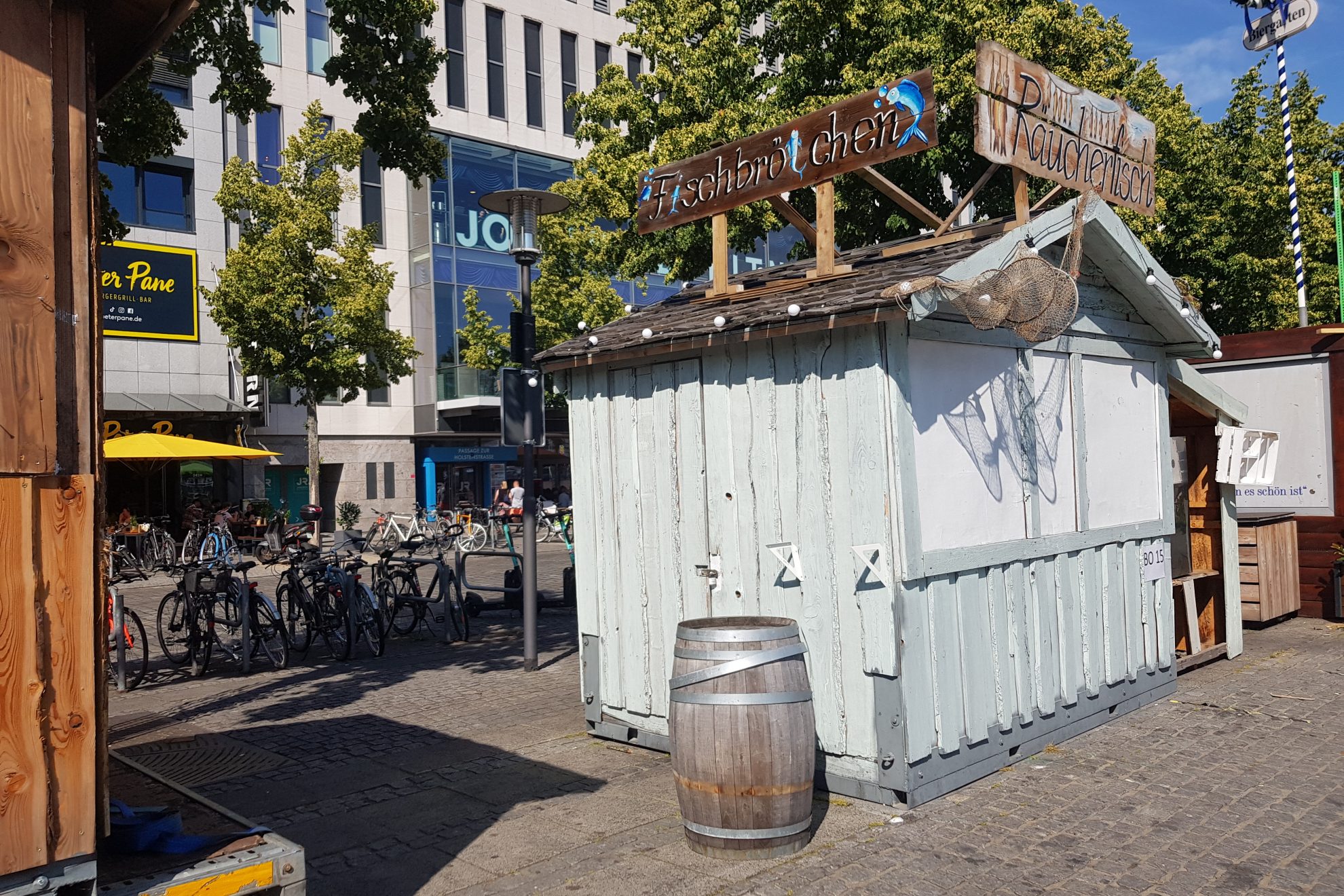 Hellgraue Holzbude mit Schildern, auf denen Fischbrötchen und Räucherfisch steht
