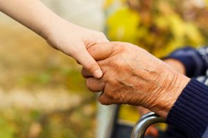 Eine große Hand mit Alterserscheinungen greift eine kleinere, jüngere Hand