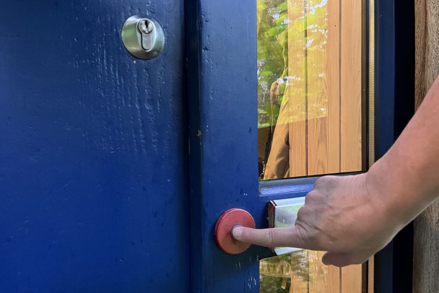 Finger drückt auf die Klingel neben einer dunkelblauen Tür