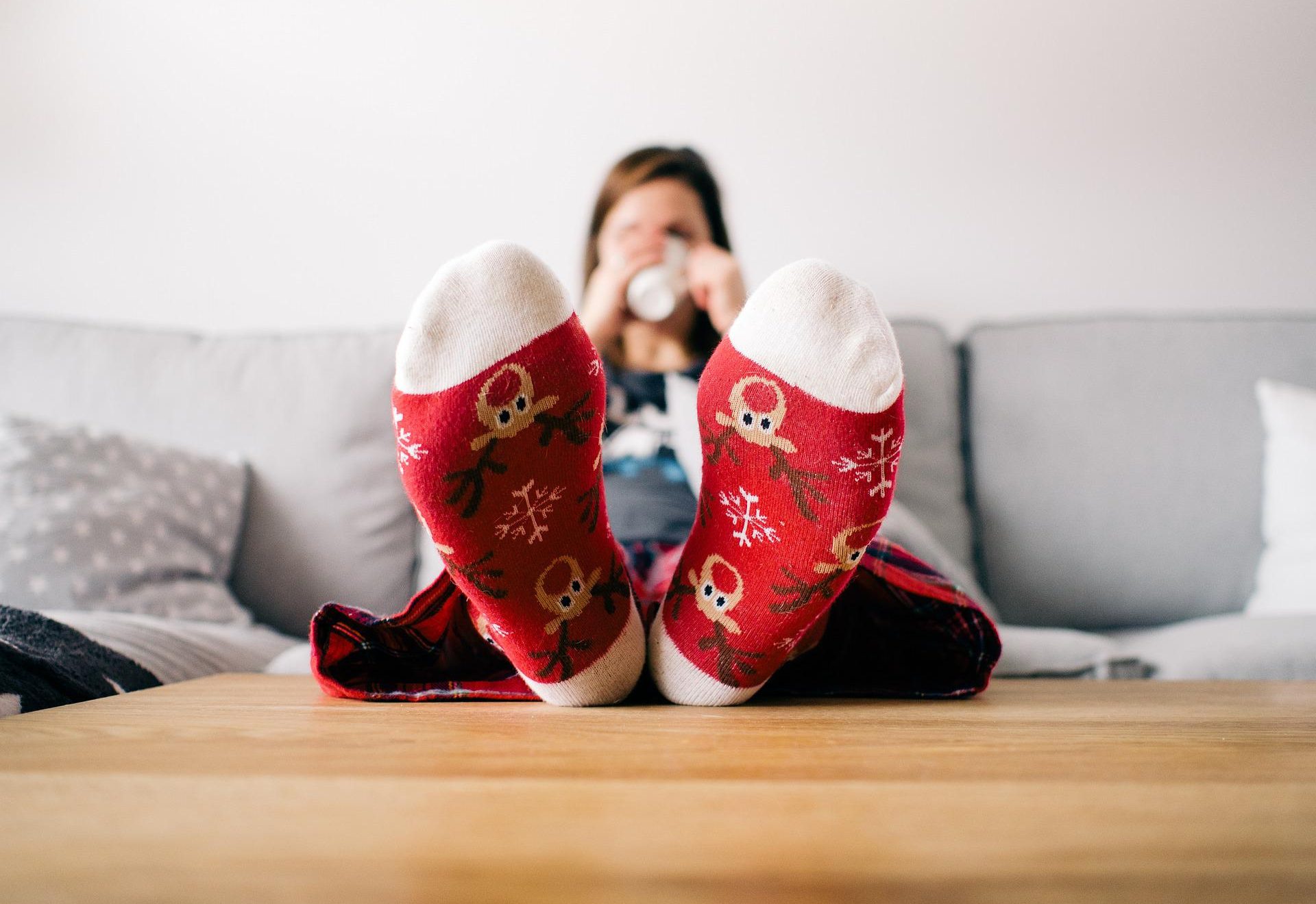 Eine Frau sitzt auf dem Sofa und streckt ihre Füße in roten Wintersocken auf einem Couchtisch aus