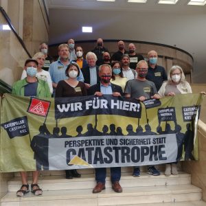 Die SPD-Ratsfraktion steht gemeinsam mit den Betriebsräten von Caterpillar auf der Treppe im Kieler Rathaus und hält ein Solidaritätsbanner