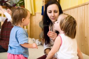 Junge Frau hält einen Kinder eine kleine Kerze hin, die es auspustet. Ein anderes Kind steht daneben und guckt zu.