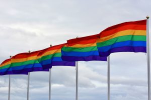 Fünf Regenbogenflaggen wehen nebeneinander, im Hintergrund wolkiger Himmel.