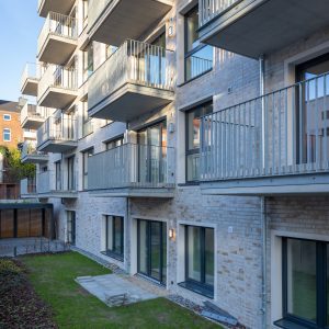 Blick von der Seite auf ein neu gebautes Wohnhaus mit Balkons, unten Rasen.