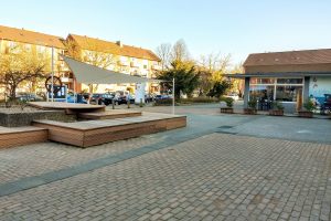 ein von Häusern umstandener Platz mit Kopfsteinpflaster und Holzbänken