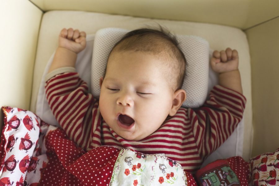 Kopf und Oberkörpers eines Babys, Baby streckt die Arme in die Luft und gähnt, hat die Augen halb geschlossen.