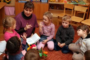 Erzieherin sitzt mit sechs Kindern im Sitzkreis auf dem Boden