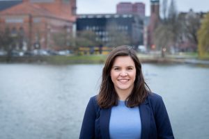 Christina Schubert vor dem Kleinen Kiel, im Hintergrund ist verschwommen das Opernhaus zu erkennen.