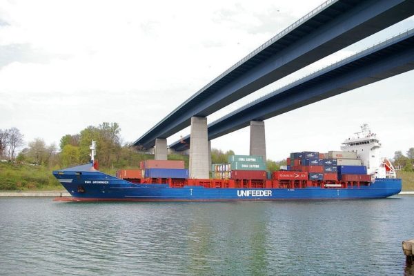 Zwei Brücken führen über eine Wasserstraße. Darunter fährt ein blaues Containerschiff
